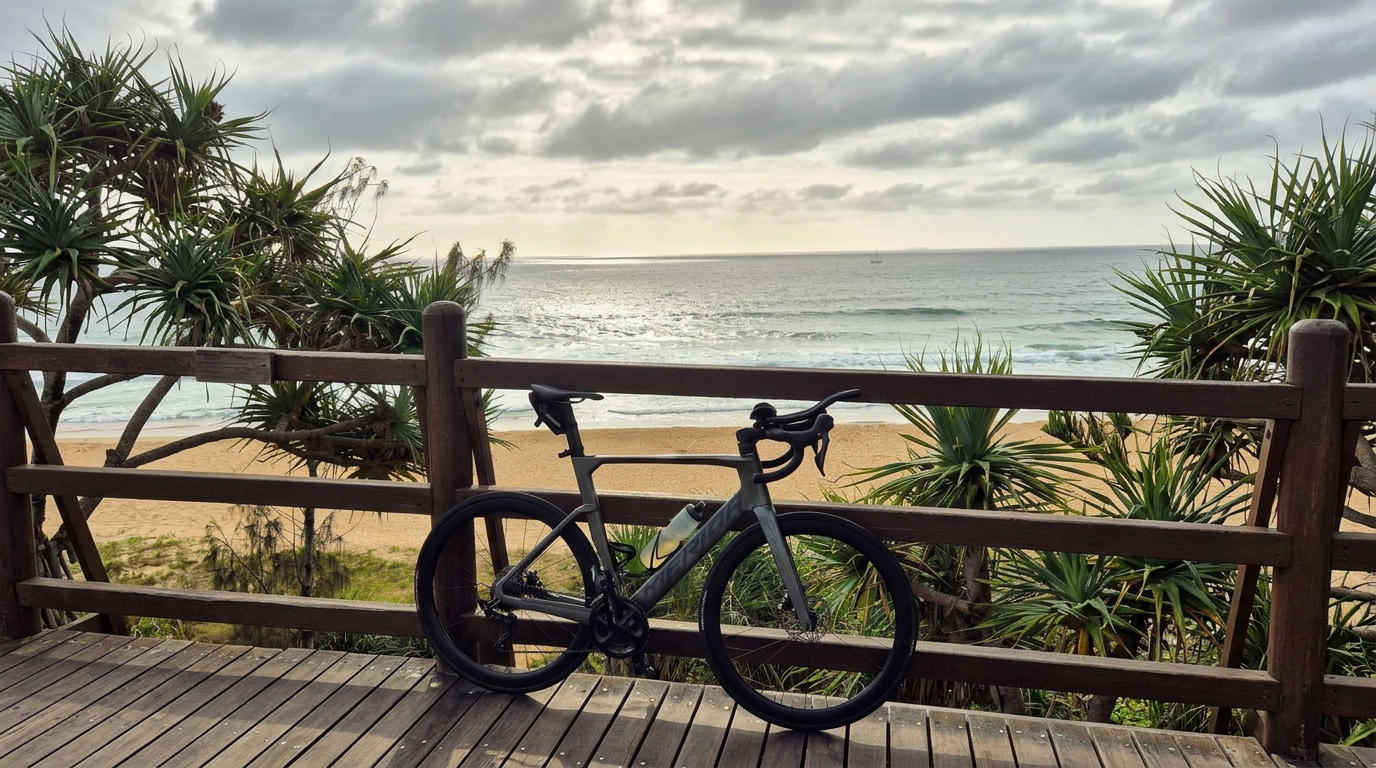 Road bike resting on a beachfront boardwalk railing with pandanus, sand and ocean beyond - Sunshine Coast cycling from Caloundra